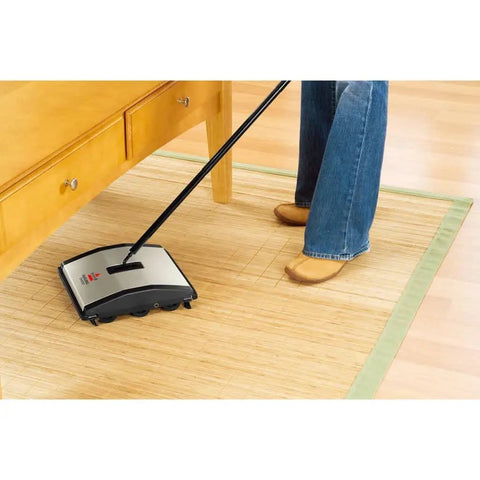 Lightweight Manual Carpet And Hard Floor Sweeper Featuring Dual Rotating Brush Roll Plus Corner Edge Brushes, operating under furniture.