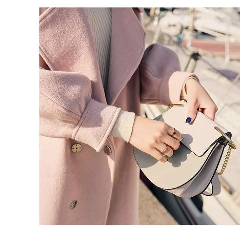 Woman in a pink coat holding a stylish grey handbag with chain details, outdoors near a marina.