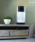 Portable Evaporative Air Cooler For Bedroom And Office Electric Standing Cooling Fan That Completely Beats The Summer Heat And Keeps You Chillin All Day Long Compact Personal Room Cooler In White on a wooden table next to a small plant.