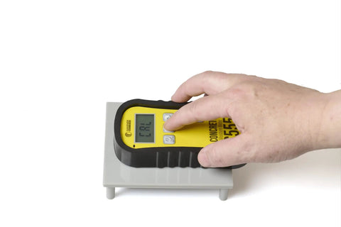 Pinless Concrete Moisture Meter For Quick Non Destructive Readings On Smooth Concrete No Surface Damage Detect Hotspots And Plan Sensor Placement With Included Standard Calibrator held on concrete block