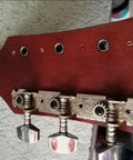 Close-up of guitar headstock with silver tuning pegs and drill holes on wood finish.