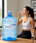 5 Gallon Water Bottle With Easy Grip Handle BPA Free Durable Plastic Jug for home on a table next to a person drinking water