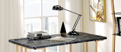Adjustable Standing Computer Desk With Built Storage And Power Port, Sleek Faux Marble Work Table For Home Office, Gold Metal Frame next to lamp and books.