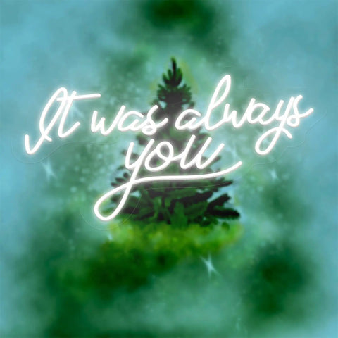 Neon sign with phrase 'It was always you' glowing over a blurred green background.
