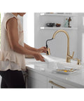 Modern Single Handle Kitchen Sink Faucet With Pull Down Spray Head And Built In Soap Dispenser, Magnetic Self Docking, Brushed Gold Finish, Single Hole Mount in use while washing a dish.