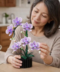 Woman assembling Purple Orchid Building Block Set With Vase, 619 Pieces, Phalaenopsis Floral Model Kit, Compatible With Lego Flowers.