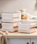 Four clear stackable trays of Big Capacity Fridge Egg Organizer With 2 Stackable Clear Trays Holds Up To 32 Eggs on kitchen counter.