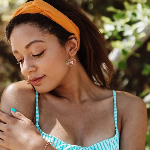 Woman wearing a striped dress with orange headband and decorative earrings, outdoors with blurred green background.