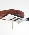 Mini stainless steel slotted spatula with black handle lifting a brownie.