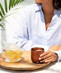 Renewed 6 Oz Smart Heated Coffee Mug With App Precision Temp Control next to a glass teapot with lemon slices.