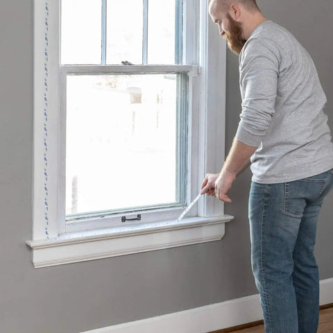 Man applying Indoor Three Window Shrink Film Insulator Kit With Crystal Clear Film 62 By 126 Inches Includes 54 Feet Double Sided Tape.