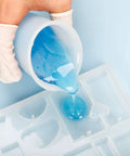 Pouring blue resin from silicone resin measuring cup tool kit with 250 ml and 100 ml cups into heart-shaped mold