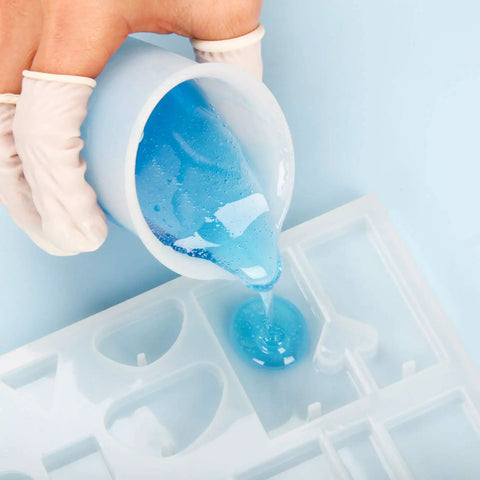 Pouring blue resin from silicone resin measuring cup tool kit with 250 ml and 100 ml cups into heart-shaped mold