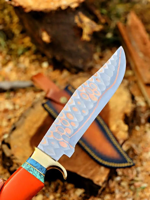 Dope Copper Damascus Fixed Blade Knife With Resin Handle showing hammered blade close-up next to leather sheath on wood