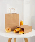 Thickened Kraft Paper Shopping Bags With Handles 60 Pack Durable Brown Paper Tote Bags For Parties Weddings Grocery Run Ready Everyday Shopping Easy Carry 26x12x31 Cm featuring two bags on a table with baguettes and juice.