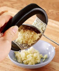 Using stainless steel garlic press rocker mincer with peeler to crush garlic into small bowl