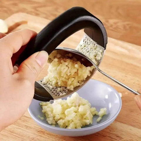 Using stainless steel garlic press rocker mincer with peeler to crush garlic into small bowl
