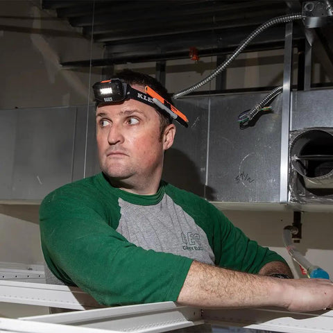 Man wearing headlamp bracket with comfy fabric strap for removable headlamps, marker and carpenter pencil holder, in a workshop.