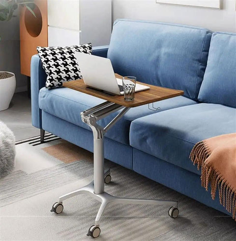 Mobile standing laptop desk with wood surface, adjustable height, and wheels on a blue sofa, ideal for sitting or standing anywhere.