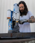 Worker using No Sweat Magnetic Drill Press with carbide cutter on steel, producing shavings at a construction site.