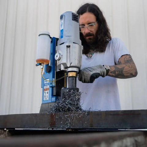 Worker using No Sweat Magnetic Drill Press with carbide cutter on steel, producing shavings at a construction site.