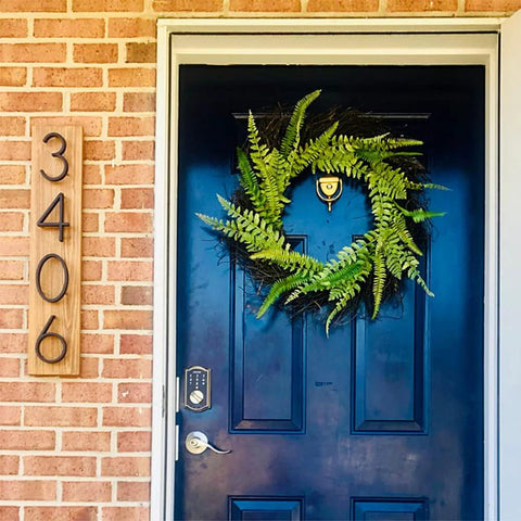Wooden address plaque with black numbers 3406 mounted on brick wall beside a blue front door.