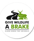 Round 5.5-inch car magnet on white with black road graphic and green deer silhouettes, Give Wildlife A Brake.
