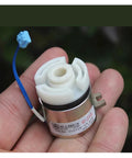 Close-up front view of a small DC24V electromagnetic clutch with white plastic rotor, metal housing, and blue wire