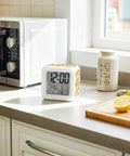 Totally Dope Digital Cube Alarm Clock With Super Responsive Silicone Buttons And A Sweet Seven Color Night Light showing time date temp on a kitchen counter.
