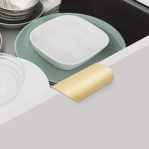 Gold Adhesive Edge Finger Pulls for Cabinets installed on drawer, 3.15 inch length, brushed gold finish, with dishes inside.