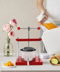 Heavy Duty Manual Fruit Wine Press Built Like A Tank Food Grade Stainless Steel Apple Grape Juicer on a table with fruits.