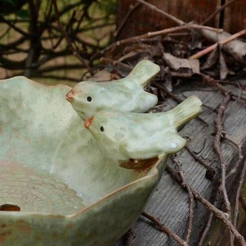 Close-up of ceramic bird bath bowl with bird figurines on edge in outdoor garden setting