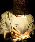 Dope 700 Lumen USB C Rechargeable EDC Flashlight clipped to cap, illuminating writing on a notebook in a dark setting