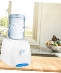 Compact Desktop Cold Water Dispenser With Easy Press Button Operation for home office use, on a kitchen counter with fruit bowl