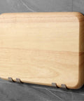 Wall-mounted wooden cutting board on gray tile wall with stainless steel hooks.
