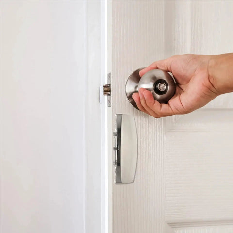 Hand using stainless steel door knob and latch on white panel for secure closure and quick access.