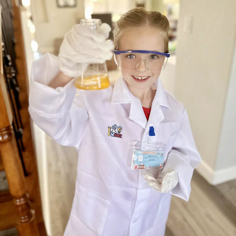 Child wearing lab coat and goggles smiling, holding a beaker with liquid, Kids Science Experiment Kit With Lab Coat Dress Up Costume And Role Play Fun.