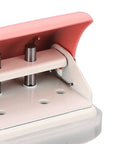Close-up of pink 3 hole punch handheld paper puncher with metal baked finish showing hole punches and metal components.