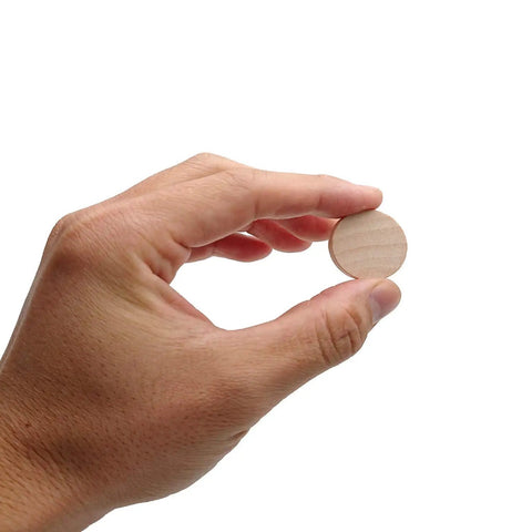 Hand holding a 1 inch unfinished round wood cookie from a 60 Pack 1 Inch Natural Wood Slices Unfinished Round Wood Cookies Real Deal Smooth Edged Pro Gear DIY Crafting Supplies Mini Wooden Disks For Paint Room Decor Makeovers.