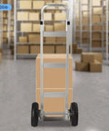Heavy Duty Aluminum Hand Truck 500lbs Capacity Steel Handle Dolly Cart Horizontal Loop Design with cardboard boxes behind.
