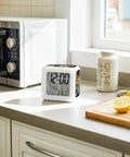 Snazzy Silent Digital Alarm Clock With Sweet Snooze And Cool Nightlight Compact Vintage Grid Cube Design Plant Vase Nightstand Piece With Temp Date Display Zero Noise Fuzz For Chill Bedrooms on kitchen counter with microwave and lemons.