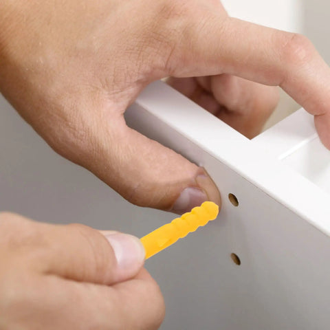 Hand inserting yellow self drilling ribbed wall plug into cabinet