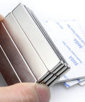 Close-up of 16-pack neodymium bar magnets with double-sided adhesive backing, 60 x 10 x 3 mm, silver metal