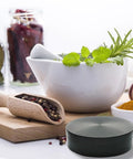 Front view of a 4-inch black herb and spice grinder on a kitchen counter with mortar and pestle and spices
