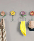 Colorful flower wall hooks for coats and towels mounted on a grey wall, featuring pink, yellow, and purple designs.