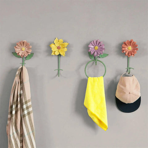Colorful flower wall hooks for coats and towels mounted on a grey wall, featuring pink, yellow, and purple designs.