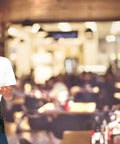 Woman wearing 12 Pack Black Waitress Aprons With 3 Pockets, Waist Aprons For Women And Men in a restaurant setting.