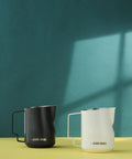 12 Oz Stainless Steel Milk Frothing Pitcher For Espresso And Latte Art Black Round Spout Milk Jug Durable Barista Grade Foam Maker Turbo Design For Rich Microfoam And Silky Smooth Latte next to a white jug.