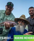 Three anglers holding a freshly caught trout, smiling at the camera with a blue sky background.