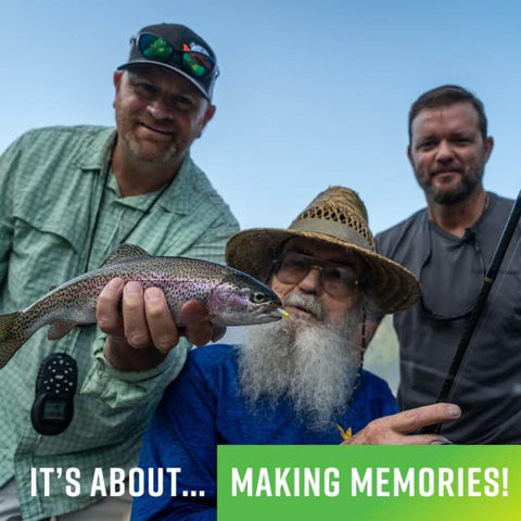 Three anglers holding a freshly caught trout, smiling at the camera with a blue sky background.